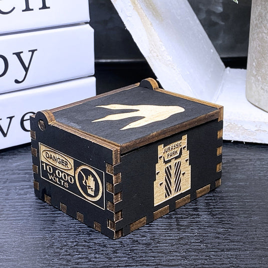 Jurassic Park: Join Alan Grant, Ellie Sattler, and Ian Malcolm on a tour of an island theme park filled with genetically resurrected dinosaurs. Get ready for an adventure with our iconic music box by MarketPlaceFad - Malaura Ashley.