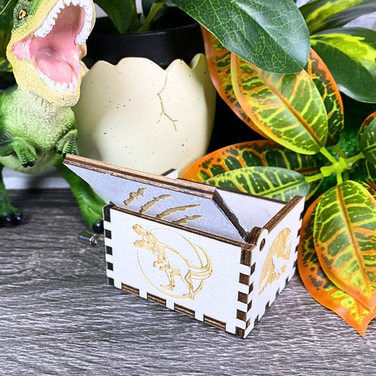 Jurassic Park: Join Alan Grant, Ellie Sattler, and Ian Malcolm on a tour of an island theme park filled with genetically resurrected dinosaurs. Get ready for an adventure with our iconic music box by MarketPlaceFad - Malaura Ashley.